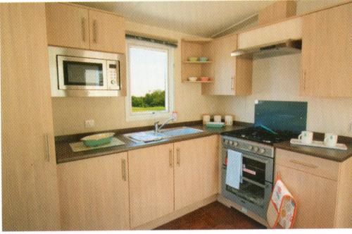 a kitchen with a sink and a stove and a microwave at Golden Burn Cottage Caravan in Padstow