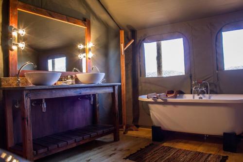 y baño con 2 lavabos, bañera y espejo. en Buffelsdrift Game Lodge, en Oudtshoorn