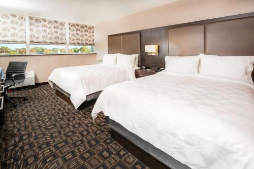 two beds in a hotel room with white sheets at Holiday Inn Louisville East - Hurstbourne by IHG in Louisville