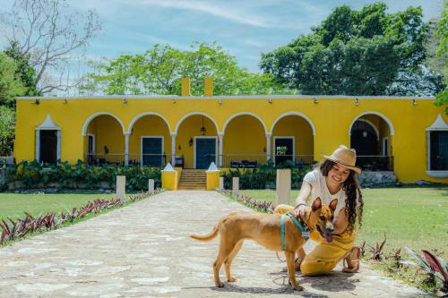 une femme avec un chien devant un bâtiment jaune dans l'établissement Hacienda San Miguel Yucatan, à Valladolid