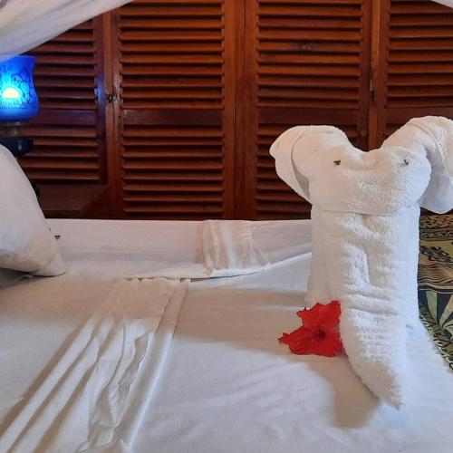 a white towel on a bed with a red flower at Kenyan House Malindi in Malindi