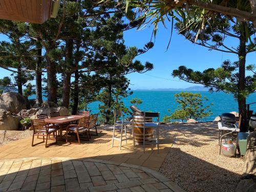 een patio met een tafel en stoelen en de oceaan bij The Boulders - Oceanfront Couple's Retreat with private pool near ferry in Nelly Bay