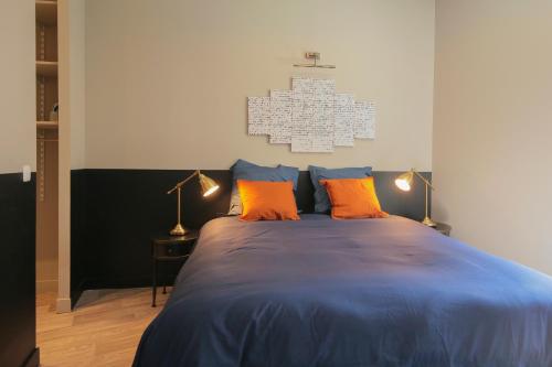 a bedroom with a blue bed with two orange pillows at Le Zen, T2 chic et cosy, wifi par SOVALFI in Saint-Étienne