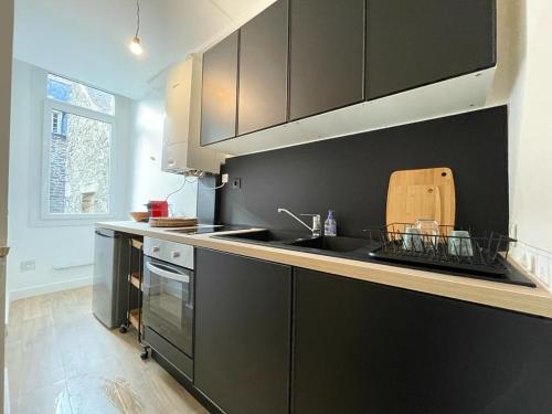 uma cozinha com armários pretos, um lavatório e um fogão em Le petit Cordelier em Dinan