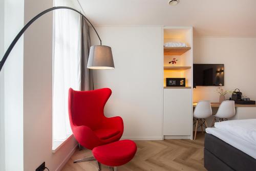una silla roja sentada junto a una ventana en un dormitorio en Snoozz Hotels Bolsward Boutique hotel zonder receptie met digitale sleutel en Bolsward