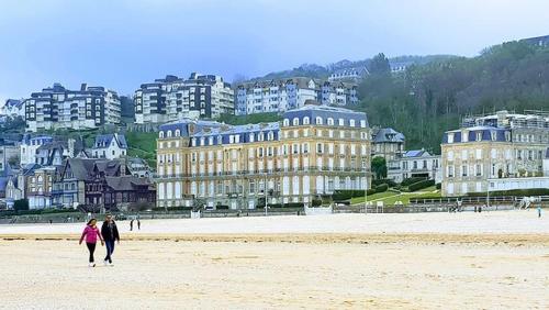 two people walking on the beach with buildings in the background at Le Parc aux Oiseaux in Le Mesnil-Simon