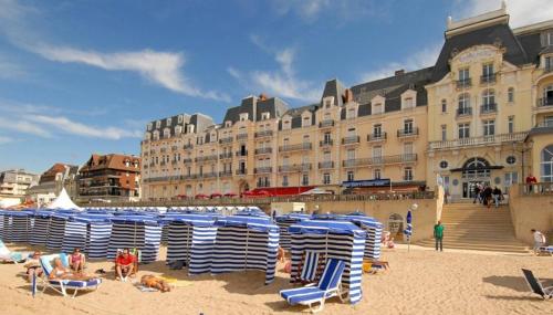 a beach with blue and white chairs and a large building at Le Parc aux Oiseaux in Le Mesnil-Simon