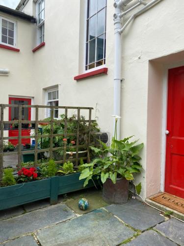 un jardín frente a una casa con una puerta roja en Coastal cottage ‘The Old Bank’ en Hartland