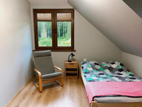 a bedroom with a bed and a chair and a window at Świerkowe Domki Cisna in Cisna