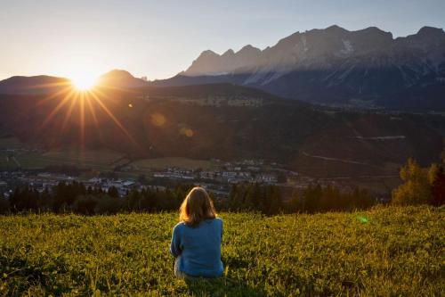 a woman sitting on a hill watching the sunset at Holzhackerin - the charming Haus am Berg in Schladming