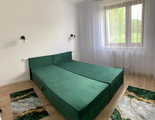 a green bed in a white room with two rugs at Apartament Wiżajny in Wiżajny