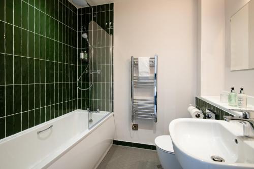 een badkamer met een wastafel, een toilet en groene tegels bij The Northallerton Inn - The Inn Collection Group in Northallerton