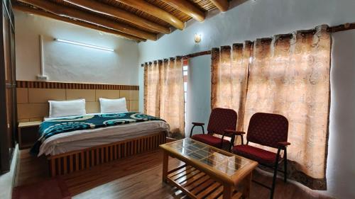 a bedroom with a bed and two chairs and a table at Serdung Guest House in Leh