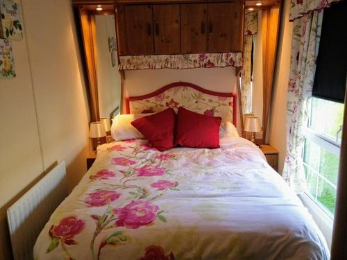 a bedroom with a bed with red pillows and a window at Cosy Cottage Caravan in Ashington