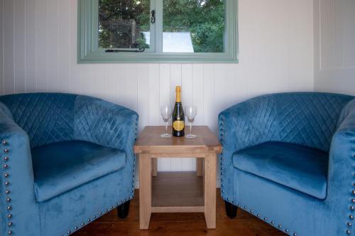 two blue chairs and a table with a bottle of wine at Rosemary - 1 Bedroom Shepherds Hut - Amroth in Amroth