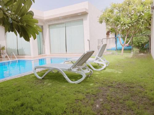two lounge chairs sitting on the grass near a swimming pool at Mooyah resort in Al Kharj