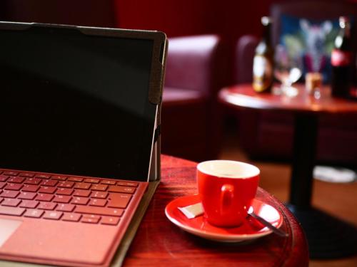 a red coffee cup sitting on a table next to a laptop at ibis Chartres Ouest Luce in Chartres