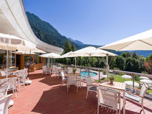 a patio with tables and umbrellas and a pool at Vivea Hotel Umhausen im Ötztal in Umhausen