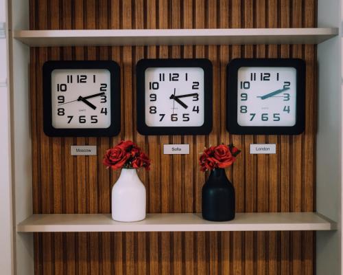 three clocks on a shelf with flowers in vases at Hotel BLVD 7 in Plovdiv