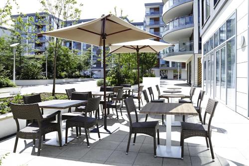 un patio al aire libre con mesas, sillas y una sombrilla en Novotel London Brentford en Brentford