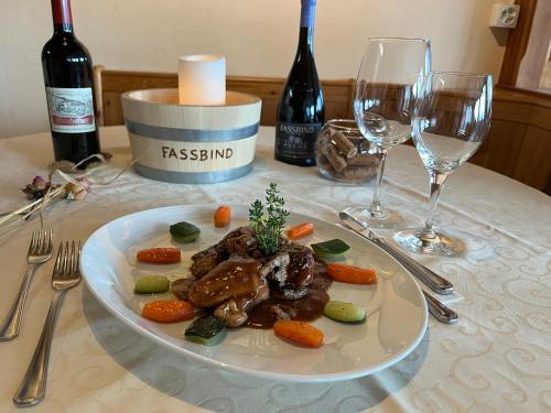 a plate of meat and vegetables on a table with wine glasses at Hotel Fassbind Beausite in Beatenberg