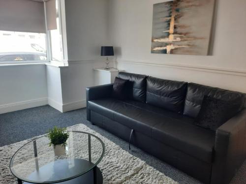 a living room with a black leather couch and a glass table at Alexander Apartments South Tyneside 2 in South Shields