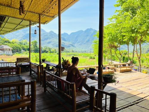 uma mulher sentada numa mesa com um portátil no alpendre em Truong Huy Homestay em Mai Châu