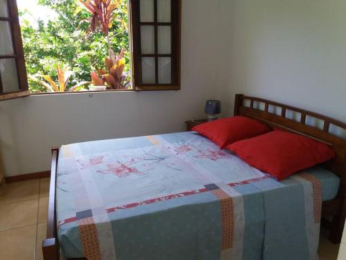 Un dormitorio con una cama con almohadas rojas y una ventana en Location saisonnière Le Clos des Agrumes, en Sainte-Anne