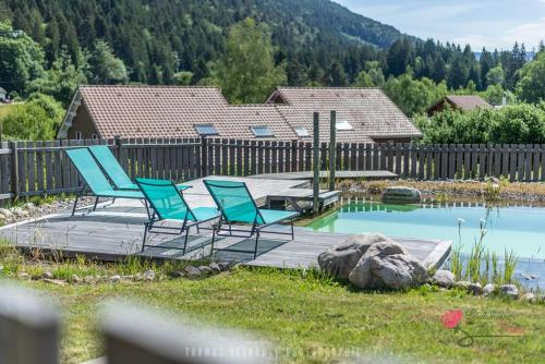 two blue chairs sitting on a deck next to a pond at Le Domaine des Fleurs - Appartement La Gentiane in Gérardmer