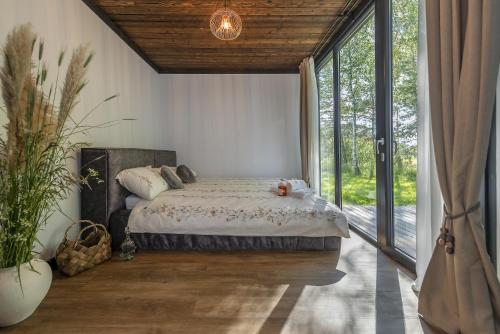 a bedroom with a bed and a large window at Modern and specious riverside cabin with hot tub in Čiobiškis