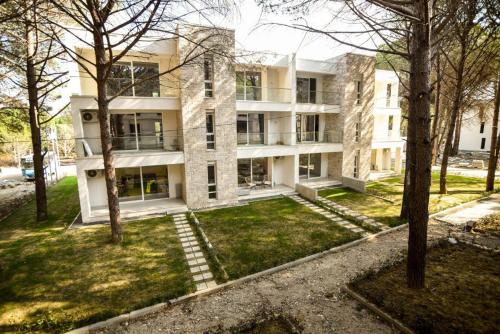un grand bâtiment blanc avec des arbres devant lui dans l'établissement Lovely 1-Bedroom Apartment at San Pietro Beach Front Resort, à Mullini i Danit