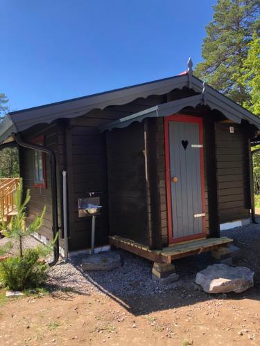 a small cabin with a red door in a yard at Timber cottages with jacuzzi and sauna near lake Vänern in Karlstad