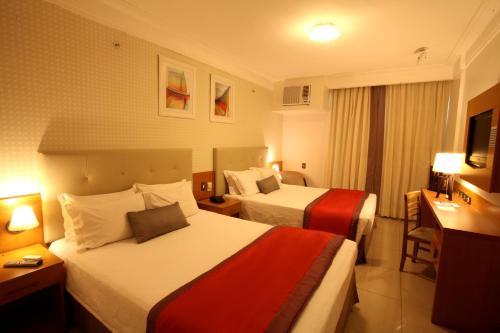 a hotel room with two beds and a desk at Royal Macaé Palace Hotel in Macaé