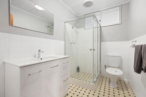 a white bathroom with a shower and a toilet at Sputnik Beach House by Experience Jervis Bay in Vincentia