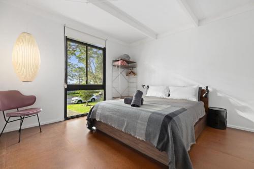 a bedroom with a bed and a chair and a window at Sputnik Beach House by Experience Jervis Bay in Vincentia