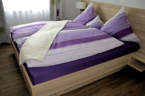 Cama con sábanas y almohadas de color púrpura y blanco en Landpension Wachtkopf Ferienwohnungen, en Vaihingen an der Enz