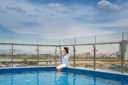 a woman sitting on the edge of a swimming pool at Santori Hotel And Spa in Da Nang