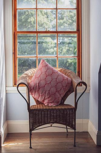 a wicker chair with a pillow sitting in front of a window at CLAYFIELD HOMESTEAD - rustic country accommodation in Bishopsbourne