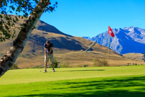 un homme jouant au golf sur un parcours avec un cerf-volant dans l'établissement Hotel le Chamois by YourAlpAdventure, à Huez