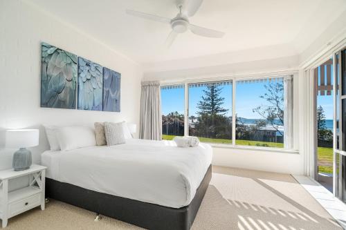 a white bedroom with a bed and large windows at Quarterdeck Unit 2 - Lennox Head in Lennox Head