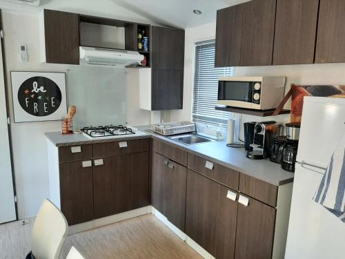 Elle comprend une petite cuisine avec des placards bruns et un évier. dans l'établissement mobile home entierement équipé, à La Roque-dʼAnthéron