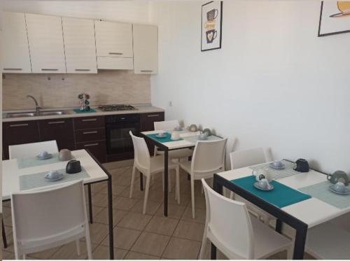 una cocina con mesas blancas, sillas blancas y fregadero en CASA VIA ALVARO, en Roccella Ionica