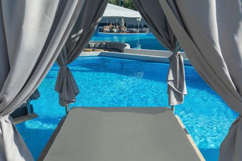 a swimming pool with blue water and curtains at Anna Hotel in Pefkohori
