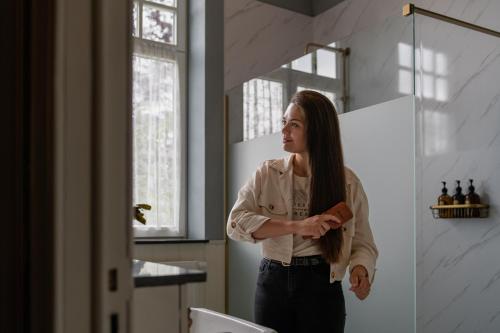 une femme debout dans une salle de bains qui se brosse les cheveux dans l'établissement Villa les Bruyères, à Dilsen-Stokkem