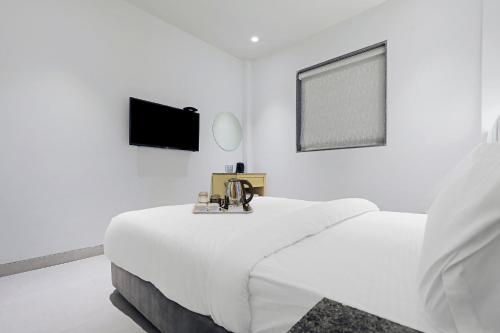 a white bedroom with a bed and a flat screen tv at FabHotel Yellow Courtyard in Bhopal