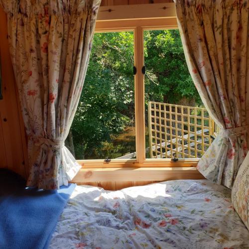 a bed in front of a window with a view at The Old Mill Shepherds Hut in Okehampton