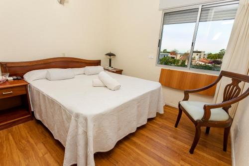 a bedroom with a bed and a chair and a window at Hotel Bahamas in Montevideo