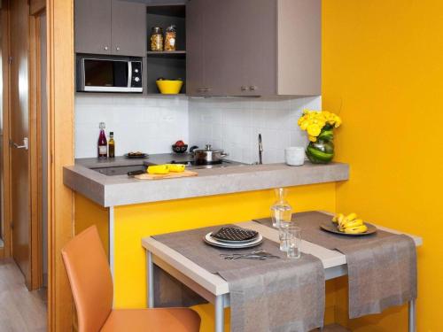 une cuisine avec des murs jaunes et un comptoir avec une table dans l'établissement Aparthotel XV Porte Versailles 2P 4 Pers Parking, à Paris