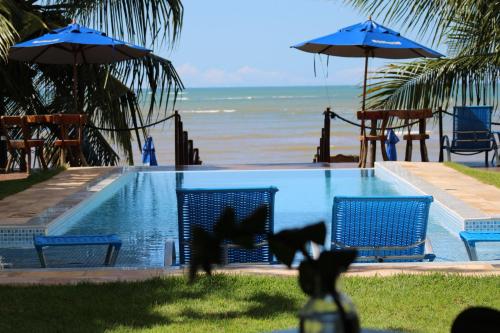 a swimming pool next to the beach with chairs and umbrellas at Sollaris Ecopousada in Japaratinga