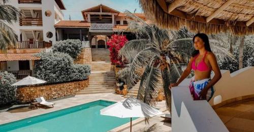 a woman sitting on a wall next to a swimming pool at Hotel & Pousada Tatajuba in Canoa Quebrada